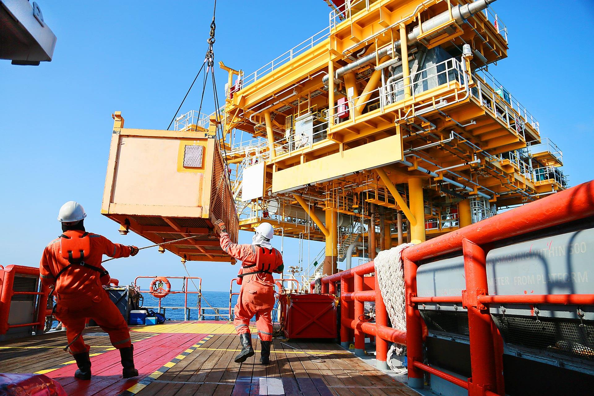 Service crew moving cargo from shipping platform to supply boat